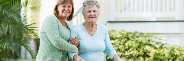 A woman helping elderly lady walk with a cane